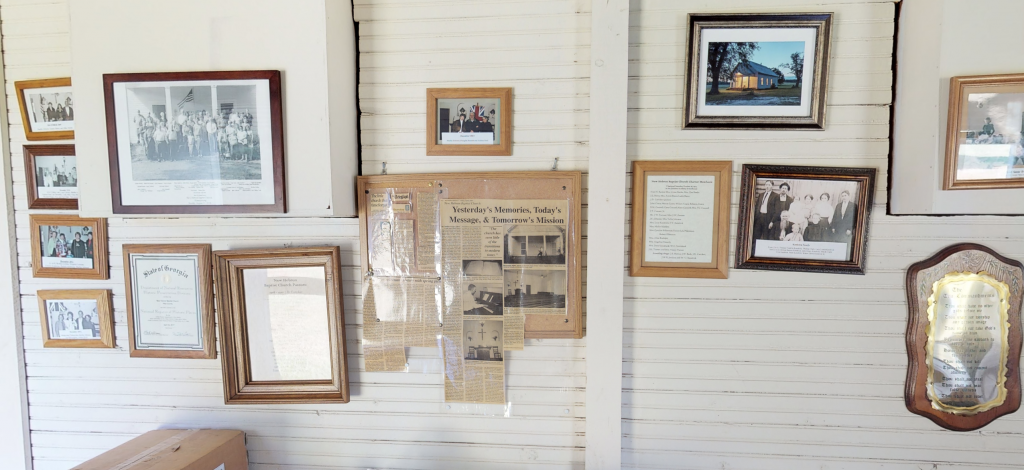 White painted wall covered with newspaper clippings, photographs, and other documents